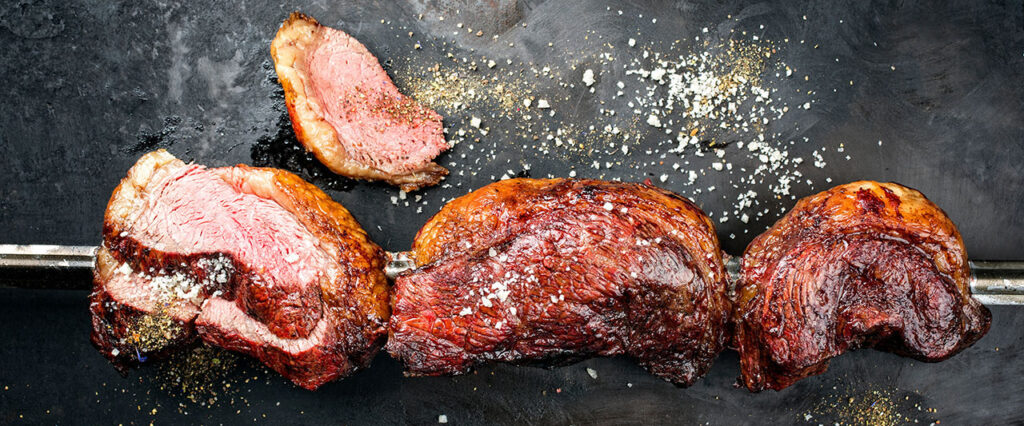Barbecue dry aged wagyu Brazilian picanha from the sirloin cap of rump beef sliced and offered as top view on a skewer on a rustic old board with copy space