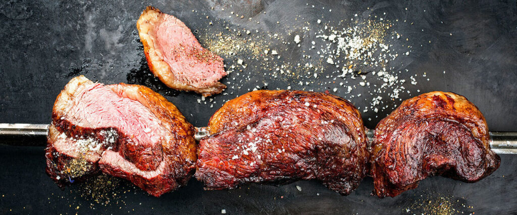 Barbecue dry aged wagyu Brazilian picanha from the sirloin cap of rump beef sliced and offered as top view on a skewer on a rustic old board with copy space